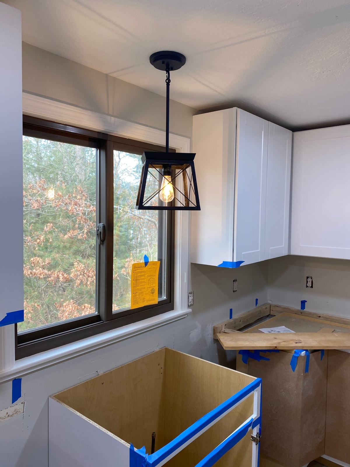 Black lantern pendant with an Edison bulb hung over a kitchen window during a remodel